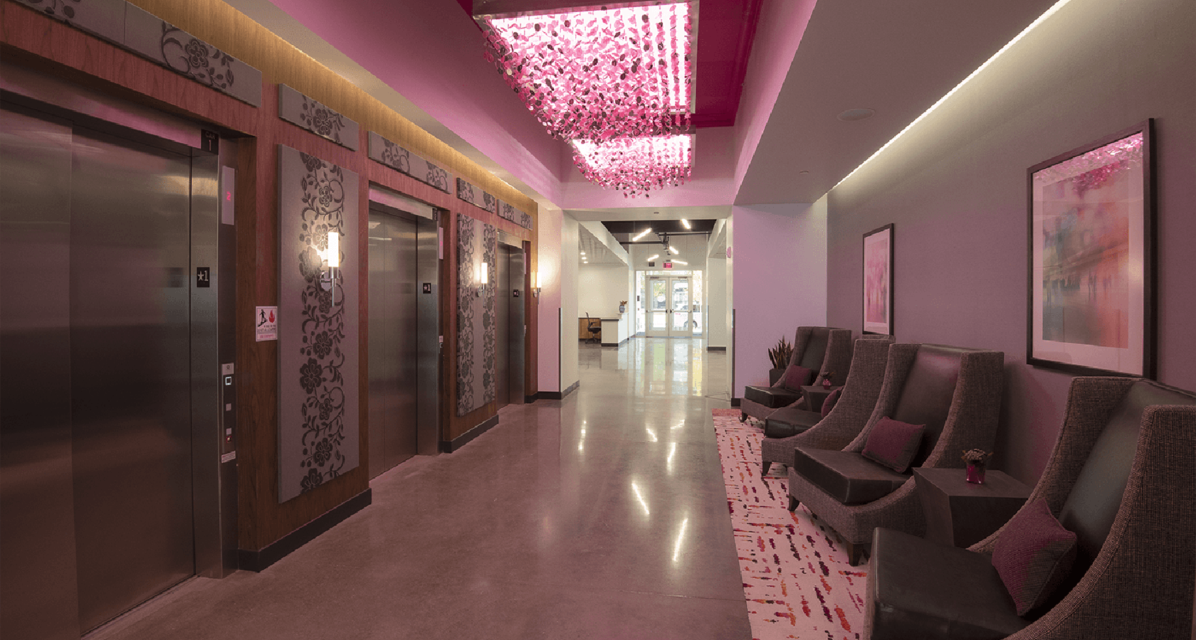 hallway with pink lighting and elevators