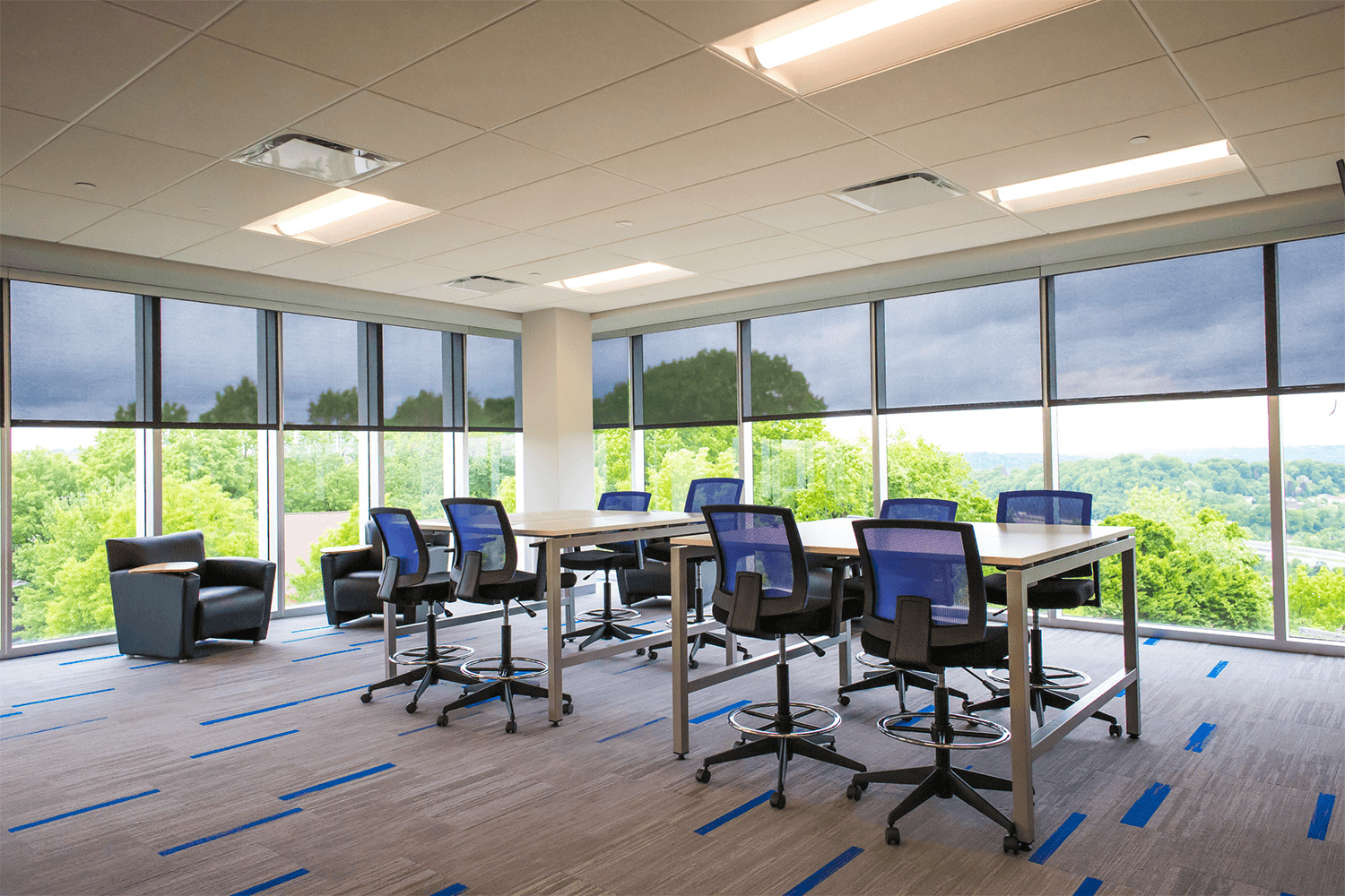 large collaborative workspace with two high-top tables and chairs, and floor-to-ceiling windows