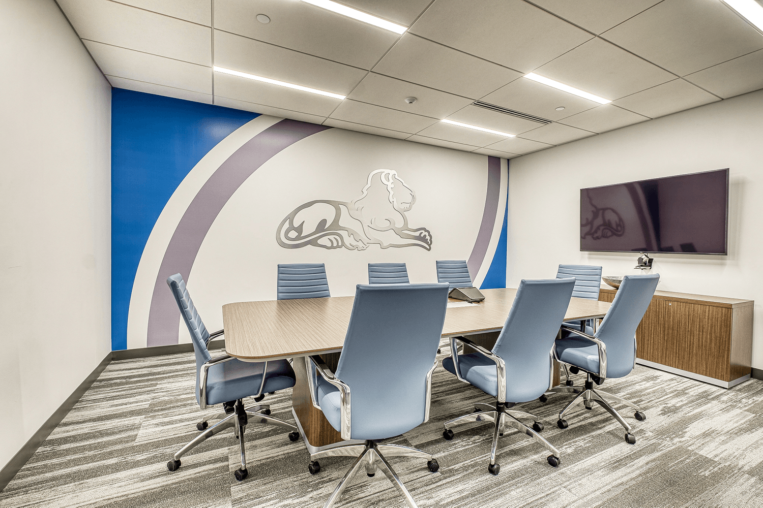conference room with blue-gray chairs, a TV, and a large wall design featuring a metal lion outline