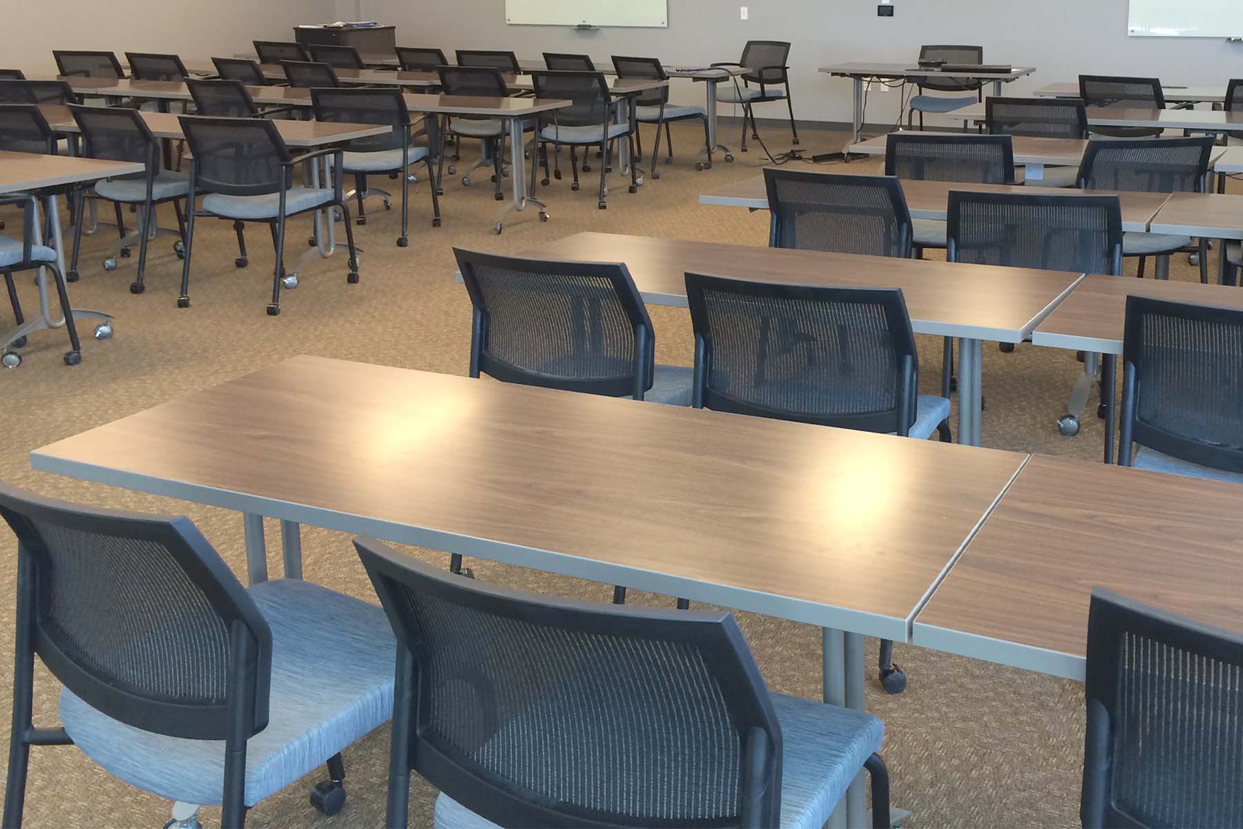 Large room with rows of desks and chairs, presentation stand and whiteboards at the front