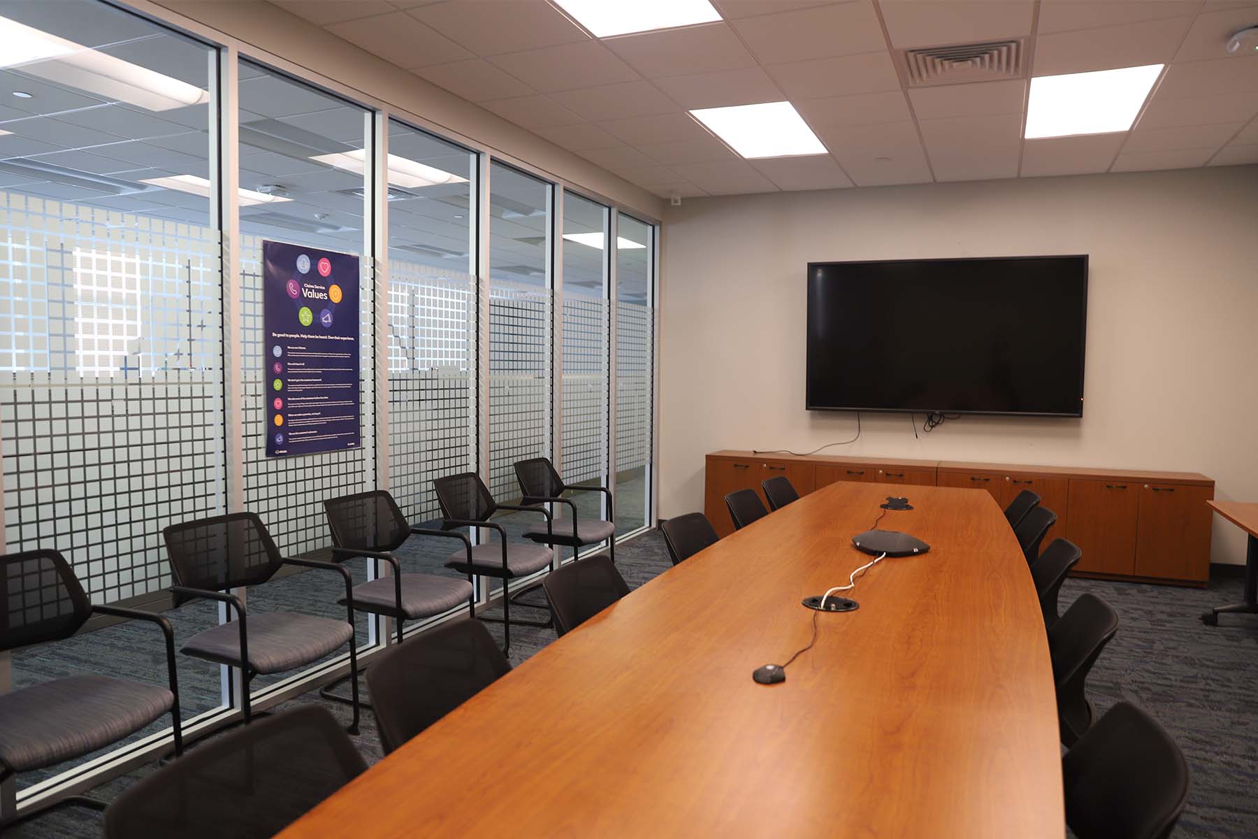 Conference room with a TV mounted on the wall, and large windows looking into open office space